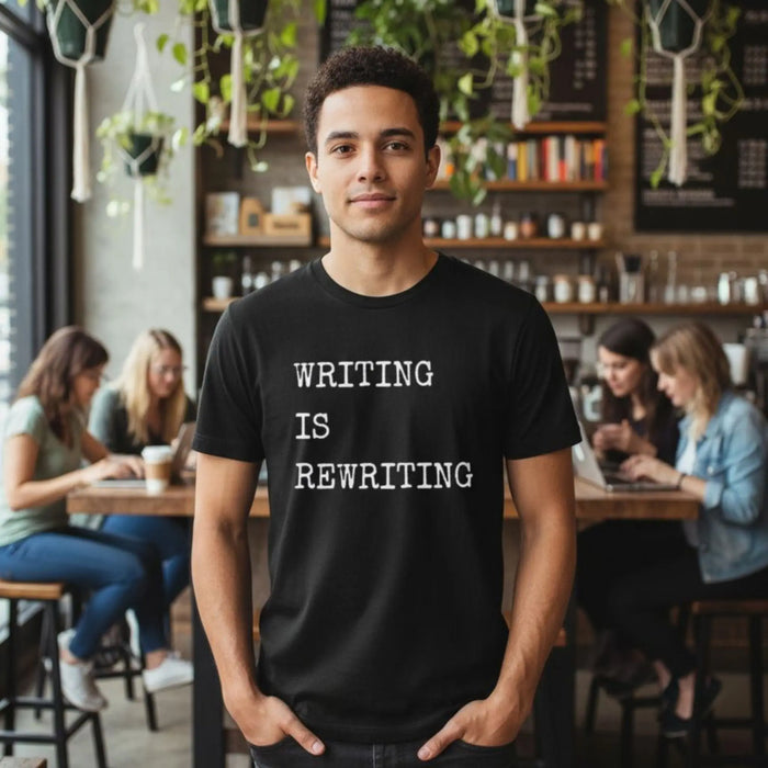 Man wearing a black t-shirt with 'WRITING IS REWRITING' text in a cafe setting.