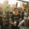 Person on a film set wearing a shirt with 'Writing is Rewriting' text, holding a coffee cup and script.
