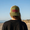 Person wearing a green cap with 'Morally Challenged' text on a beach