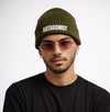 Man wearing a green beanie with 'ANTAGONIST' text and pink sunglasses on a white background