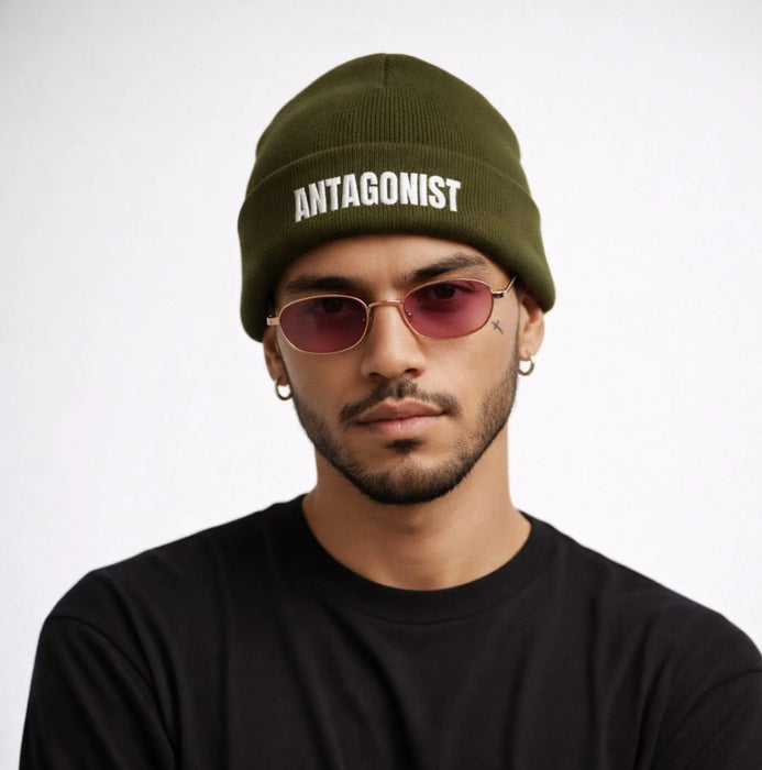 Man wearing a green beanie with 'ANTAGONIST' text and pink sunglasses on a white background