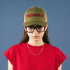 Person wearing a green cap with 'PROTAGONIST' text and a red crop top against a blue background