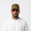 Man wearing a green cap with 'Protagonist' text, red sunglasses, and a white t-shirt on a white background