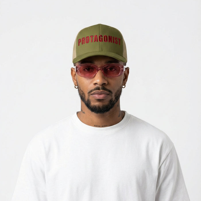 Man wearing a green cap with 'Protagonist' text, red sunglasses, and a white t-shirt on a white background
