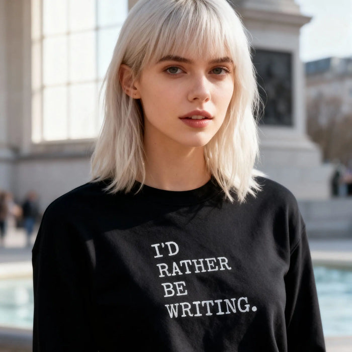 Person wearing a black sweatshirt with 'I'd Rather Be Writing' text, standing outdoors.