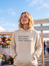 A woman wearing a cream-colored hoodie with the text 'READ BOOKS. WALK DOGS. FIGHT FASCISTS.