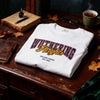 Folded white t-shirt with 'Wuthering Heights' print on a wooden desk with books and a cup of tea.
