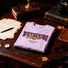Pink t-shirt with 'Wuthering Heights' text on a wooden desk with vintage items.