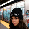 Woman wearing a black beanie with 'PLOT TWIST' text in a subway setting with graffiti.