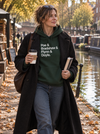 A woman walking along a canal path in autumn, wearing a dark green hoodie with the text 'Poe & Bradshaw & Flynn & Doyle.' in white.
