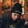 woman wearing an UNRELIABLE NARRATOR beanie writing on a notebook in a cafe